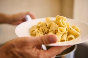 Close-up pouring Italian pasta on white plate before plating up and serving to the customers. Chef holds plate with freshly cooked Italian pasta photo