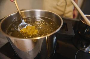 Close-up mixing Italian pasta in a boiling water, preparing spaghetti to the condition Al Dente. Chef cooking pasta, standing at electric stove or induction cooker. Extreme closeup photo