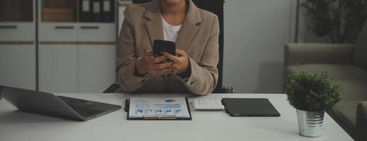 Young happy business woman, smiling pretty professional businesswoman worker looking at smartphone using cellphone mobile technology working at home or in office checking cell phone sitting at desk. photo