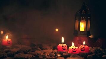 Halloween sfondo, 3 a forma di zucca candele nel il primo piano, un vecchio lampada su un' roccia contro un' blu sfocato sfondo con giallo luci e foschia video