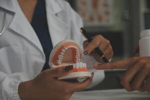 Concentrated dentist sitting at table with jaw samples tooth model and working with tablet and laptop in dental office professional dental clinic. medical doctor working photo