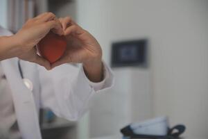 manos de médico mujer participación rojo corazón, demostración símbolo de amar, humano apoyo a paciente, promoviendo médico seguro, temprano chequeo para cuidado de la salud, cardiólogo ayuda. cerca arriba de objeto foto