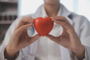 manos de médico mujer participación rojo corazón, demostración símbolo de amar, humano apoyo a paciente, promoviendo médico seguro, temprano chequeo para cuidado de la salud, cardiólogo ayuda. cerca arriba de objeto foto