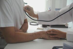 joven médico es utilizando un estetoscopio escucha a el latido del corazón de el paciente. Disparo de un hembra médico dando un masculino paciente un cheque arriba foto