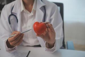 Hands of doctor woman holding red heart, showing symbol of love, human support to patient, promoting medical insurance, early checkup for healthcare, cardiologist help. Close up of object photo