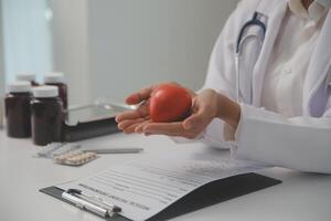 Hands of doctor woman holding red heart, showing symbol of love, human support to patient, promoting medical insurance, early checkup for healthcare, cardiologist help. Close up of object photo