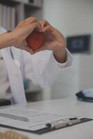 Hands of doctor woman holding red heart, showing symbol of love, human support to patient, promoting medical insurance, early checkup for healthcare, cardiologist help. Close up of object photo