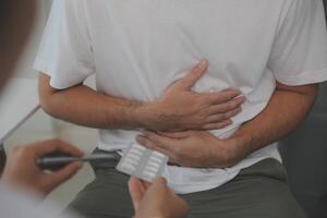 Man suffering with severe stomach pain sitting at home. Hand of mature guy holding abdomen suffering from ache, diarrhea or indigestive problem. Caucasian guy pressing on belly on painful sensation photo