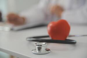 Hands of doctor woman holding red heart, showing symbol of love, human support to patient, promoting medical insurance, early checkup for healthcare, cardiologist help. Close up of object photo