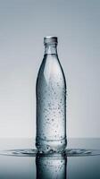 A glass bottle filled with mineral sparkling water rests on a glass table photo