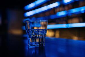 A glass of water sits on a bar counter. The bar is dimly lit, giving the scene a cozy and intimate atmosphere. photo