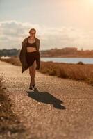 Portrait blonde sea cape. A calm young blonde in an unbuttoned khaki raincoat walks along the seashore, under a raincoat a black skirt and top photo