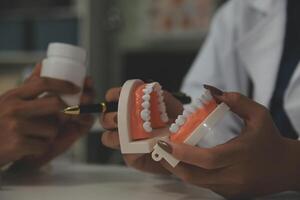 dentista concentrado sentado en la mesa con muestras de mandíbula modelo de diente y trabajando con tableta y computadora portátil en el consultorio dental clínica dental profesional. medico trabajando foto