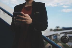 Young asian woman in international airport, using mobile smartphone and checking flight at the flight information board photo