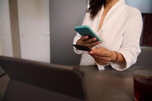 Close-up view of a woman holding blank black credit card, using mobile phone, transferring money via internet banking, making payment, using mobile app. Copy advertising space photo
