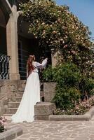 a beautiful woman in a white flowing long dress stay near a beautiful field with pink flowers rear view photo