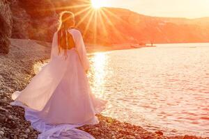 misterioso mujer silueta largo pelo camina en el playa Oceano agua, mar ninfa viento escucha a el ola. lanza arriba un largo blanco vestido, un adivinar puesta de sol. artístico foto desde el espalda sin un cara