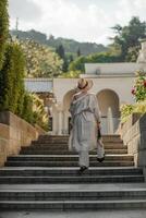 Woman on the stairs in the park. A middle-aged lady in a hat in a white outfit with a bag walks around the Livadia Palace photo