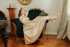 mature woman in a beautiful beige dress sits elegantly on a green armchair photo