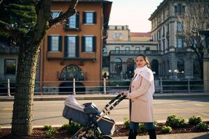 Attractive Caucasian woman, loving mother in warm clothes enjoys a walk with her baby sleeping in baby carriage, admiring the beautiful city of Como in Italy. People, lifestyle and tourism photo