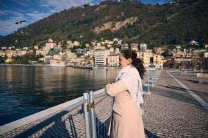 contento joven mujer en el paseo, contemplando el lago de venir, relajante al aire libre terminado alpino montañas fondo, en un soleado invierno día. personas y belleza en naturaleza. Italia. viaje destinos foto