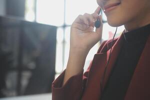 Friendly female helpline operator in call center. Young woman working in call center and holding microphone on headset with hand. photo