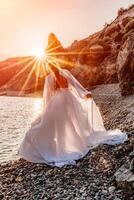 misterioso mujer silueta largo pelo camina en el playa Oceano agua, mar ninfa viento escucha a el ola. lanza arriba un largo blanco vestido, un adivinar puesta de sol. artístico foto desde el espalda sin un cara