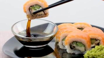 Philadelphia sushi zwart bord, zwart eetstokjes, soja saus, wit achtergrond, detailopname van sushi Aan een zwart achtergrond video