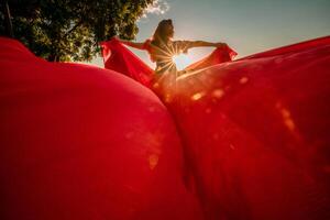 Sunrise red dress. A woman in a long red dress against the backdrop of sunrise, bright golden light of the sun's rays. The concept of femininity, harmony. photo