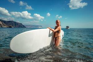 Woman in black bikini sap sea. Portrait of a happy girl on the background of a surfboard in the sea on a sunny summer day photo