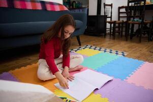 Lovely little child girl sitting on a colorful puzzle carpet, studying from home, doing homework. People. Kids. Education concept photo