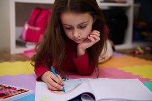 Adorable little child girl drawing rainbow with pastel pencils, lying on a multicolored puzzle carpet in her room at home. Art and creativity concept. Kids development, education. Hobbies and leisure photo