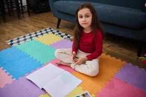 Adorable elementary age child, little school girl at home, doing homework, writing on copy book, smiling looking at camera photo