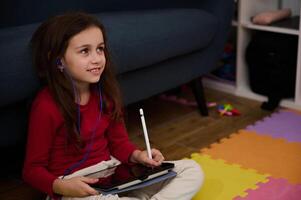 Adorable little child girl holding digital tablet and white stylus, learning online, doing homework, drawing pictures, watching cartoons or listening to online webinar class. Kids and technology photo