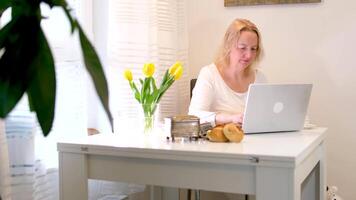 donna seduta nel camera parlando su Telefono su il computer portatile Lavorando potabile caffè libero professionista opera in linea studia tempo libero chat con amici piacevole mattina quotidiano processi pensiero sognare meraviglioso vita video