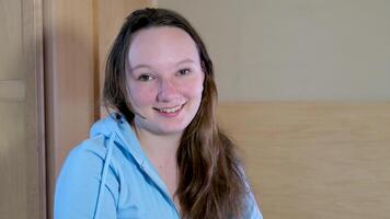 a teenage girl with unwashed hair in a room in a blue blouse looks into the frame shakes her head in agreement smiling round face of a teenager video