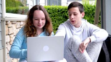 jongens tiener- meisjes aan het doen online klassen taak aan het kijken film sociaal netwerken internet levendig chatten emoties oprechtheid tiener jongen lachend omklemd handen in de omgeving van zijn knieën meisje Holding laptop video