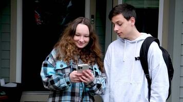adolescentes falando olhando às a telefone mostrando social redes de outros contas perfis fotos surpreso menina rindo tímido humorístico comunicação pasta escolares menino-adolescente-menina adolescente video