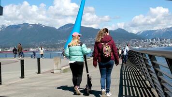 Canada Place two girls with a scooter walk along the embankment go to the statue a drop a backpack on back of tourist travel nicks of another country canadians high mountains white clouds on blue sky video