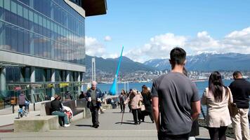 Canadá Lugar, colocar contra a pano de fundo do a estátua do uma solta dentro Vancouver, pessoas estão caminhando ao longo aterro velho homem segurando bebidas para mulher bastão atrasado atrás pessoas andar sentar em bancos levar foto video