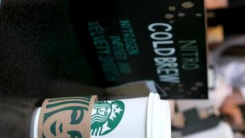 Starbucks preparando café de varios bebidas detrás mostrador mujer blanco camiseta delantales y enmascarado vendedores en lentes de asiático-europeo etnia niña echar un vistazo en a tomar café latté escaparate emisión video