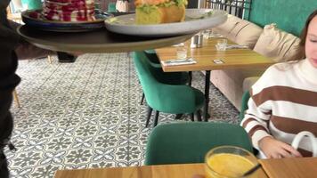 tjänande i restaurang orange juice pannkakor med frukter, bär kokos flingor som väl som lunch ägg med rostat bröd räka och avokado flicka i randig Tröja Sammanträde på trä- tabell väntar för frukost video
