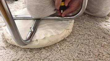repairing a stool, a man screws a bolt into the stool legs, attaching them to the base, sportswear, at home on a white carpet, the hands of an adult man, doing housework, homemade repairs video