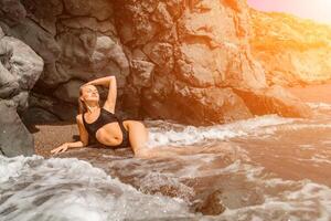 Woman swimsuit sea. Attractive blonde woman in a black swimsuit enjoying the sea air on the seashore around the rocks. Travel and vacation concept. photo