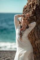 Middle aged woman looks good with blond hair, boho style in white long dress on the beach decorations on her neck and arms. photo