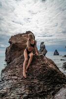 mujer traje de baño mar. atractivo rubia mujer en un negro traje de baño disfrutando el mar aire en el costa alrededor el rocas viaje y vacaciones concepto. foto