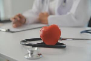 Hands of doctor woman holding red heart, showing symbol of love, human support to patient, promoting medical insurance, early checkup for healthcare, cardiologist help. Close up of object photo