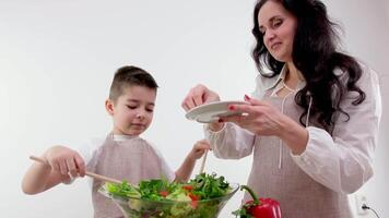 pretty housewife looks at little son tearing fresh lettuce leaves to cook salad at table in light modern kitchen at home video