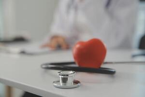 Hands of doctor woman holding red heart, showing symbol of love, human support to patient, promoting medical insurance, early checkup for healthcare, cardiologist help. Close up of object photo