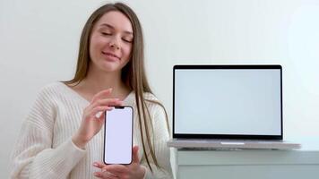Be H3althy beautiful cute young woman holding a phone in hands with white screen for advertising nea laptop space for text beautiful neutral person office worker subordinate tenderness beauty youth video